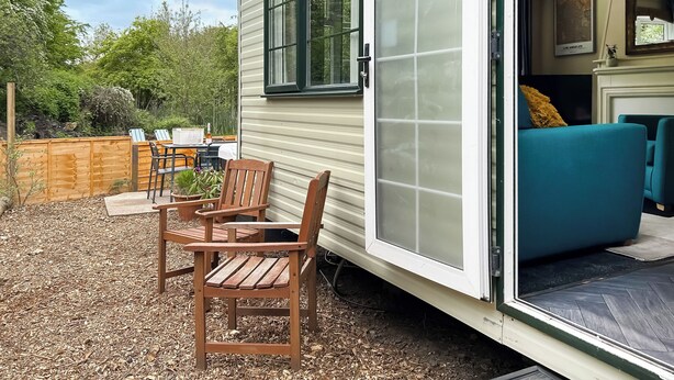 A mobile home with a patio area, a dining table, chairs, and a blue sofa inside. - Station House Retreat (Royston)