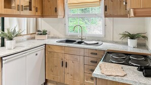 A kitchen with wooden cabinets, a sink, a stove, and two potted plants. - Station House Retreat (Royston)