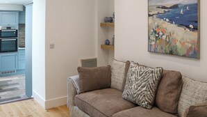 A living room with a sofa, a painting, and a kitchen area with blue cabinets and an oven. - Platform 1 - Uk51994 (Haverfordwest)