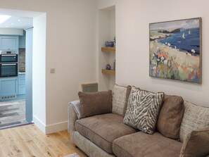 A living room with a sofa, a painting, and a kitchen area with blue cabinets and an oven. - Platform 1 - Uk51994 (Haverfordwest)