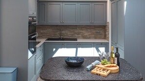 A modern kitchen with grey cabinets, a built-in oven, a sink, and a breakfast bar with a bowl and snacks. - Platform 1 - Uk51994 (Haverfordwest)