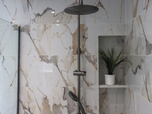 A shower with a rain showerhead, a handheld showerhead, and a potted plant in a bathroom with marble walls. - Platform 1 - Uk51994 (Haverfordwest)