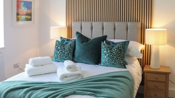 A neatly made bed with pillows, a bedside lamp, and a small wooden nightstand. - Platform 1 - Uk51994 (Haverfordwest)
