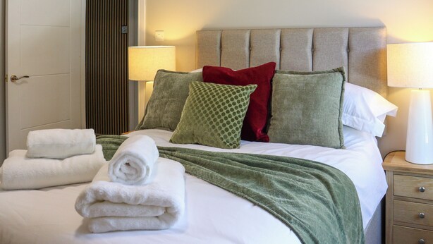 A neatly made bed with pillows, a green throw blanket, and folded towels. - Platform 2 - UK51996 (Haverfordwest)