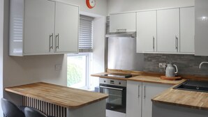 A modern kitchen with white cabinets, a built-in oven, a coffee maker, and a window with blinds. - Platform 2 - UK51996 (Haverfordwest)