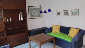 A living room with a wooden cabinet, a sofa with patterned cushions, a wooden coffee table, and three wall-mounted pendant lights.