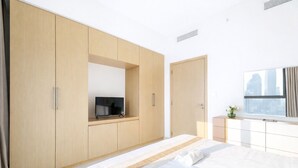 Een moderne slaapkamer met een groot bed, een tv bevestigd aan een houten kast, en een raam met uitzicht op de stad.