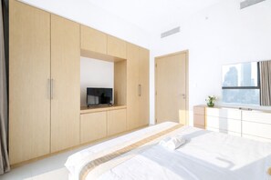 Ein modernes Schlafzimmer mit einem großen Bett, einem an einer Holzkommode befestigten Fernseher und einem Fenster mit Blick auf die Stadt.