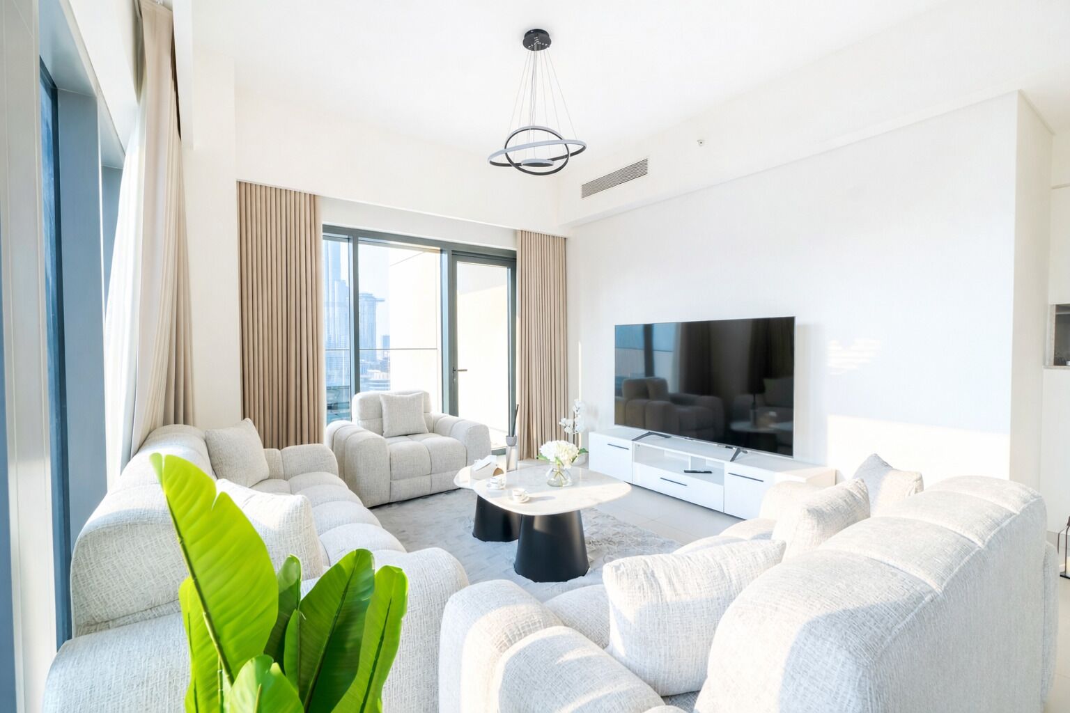 A modern living room with a large flat-screen TV, a sectional sofa, and a coffee table.