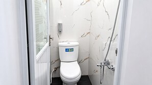 A compact bathroom with a toilet, a shower, and a marble wall. - Sekuto Inn by Sawala (Tegal)