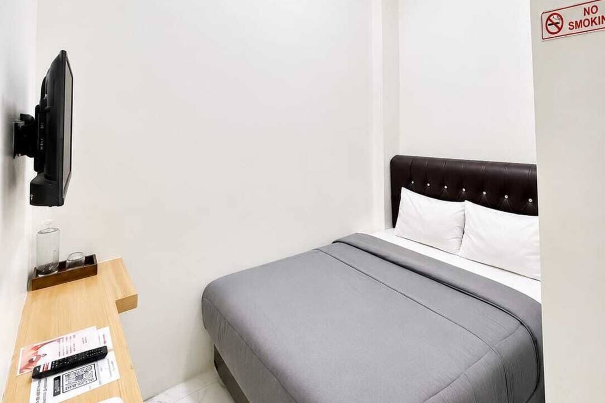 Quarto de hotel com uma cama, televisão fixada na parede, uma janela e placa indicando proibido fumar.