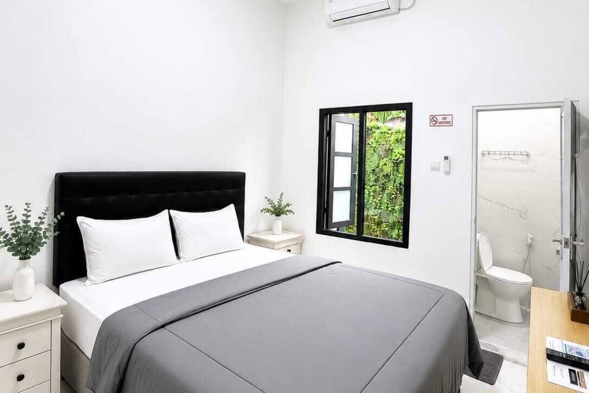 Quarto moderno com cama, mesa de cabeceira e vista para o verde lá fora.