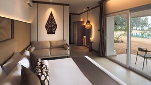 A modern hotel room with a large bed, a sofa, a dining area, and a view of a beach.
