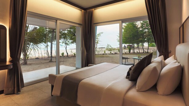 A bedroom with a bed, curtains, a TV, and a view of the beach.