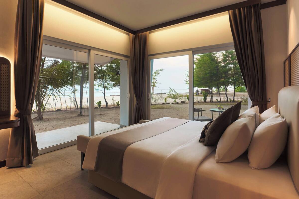 Ein Schlafzimmer mit Bett, Vorhängen, Fernseher und Blick auf den Strand.