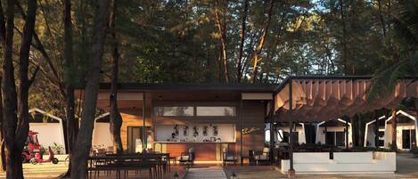 Un café moderno al aire libre con estructura de madera, asientos y un sendero que lleva a un edificio con zona de bar.