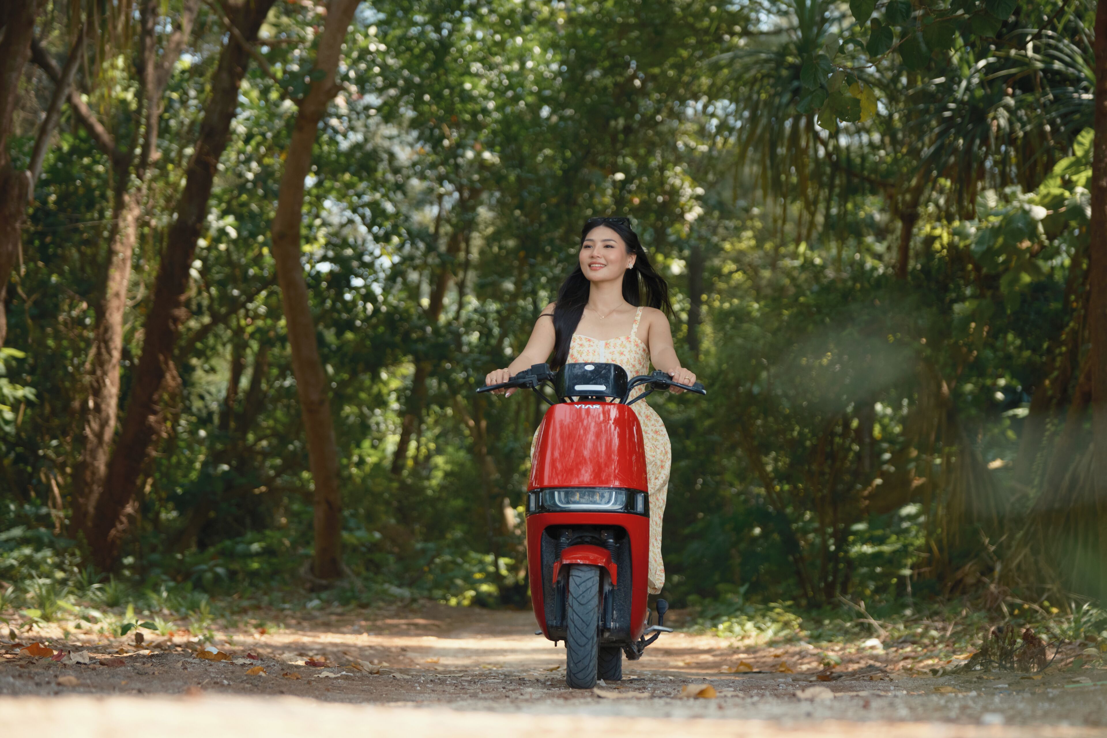 A person riding a red scooter on a dirt path surrounded by trees.