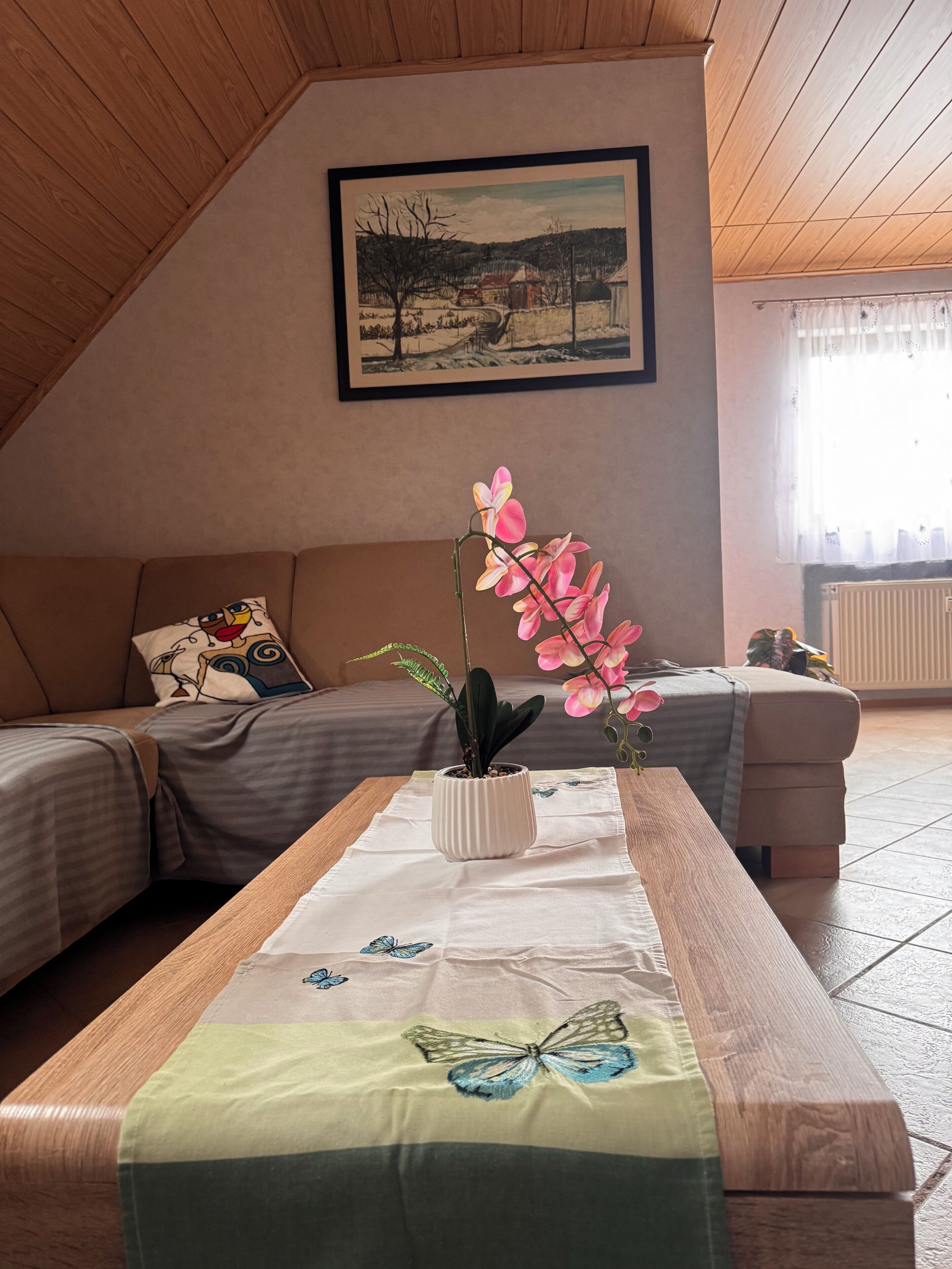 A cozy room with a wooden ceiling, a painting on the wall, a sofa, a table with a butterfly tablecloth, and a potted orchid.. Quiet designer apartment with whirlpool tub, steam shower, and nature