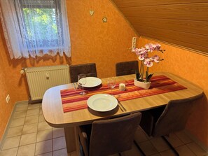 En spiseplads med et bord dækket til to personer, en radiator og et vindue med blondegardiner.