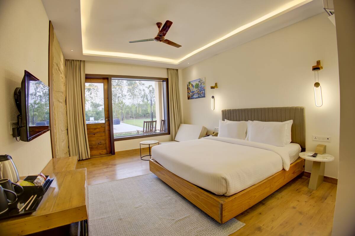 A modern hotel room with a large bed, a desk, a ceiling fan, and a view of the outdoors.