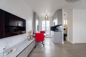 A modern kitchen with a dining area, a red chair, and a pendant light. - Eiffel Tower View Studio w/ Balcony & Elevator (Paris)