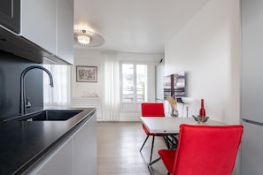 A modern kitchen with a black sink, a dining area with red chairs, and a white table. - Eiffel Tower View Studio w/ Balcony & Elevator (Paris)