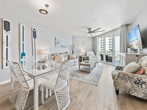 A modern living room with a glass dining table, white chairs, a sofa, a coffee table, and a ceiling fan. - Spacious 3-bedroom apartment in gorgeous Destin with AC (Destin)