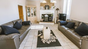 A living room with two leather sofas, a fireplace, a wooden cabinet, and a tiled floor. - Annie's Cottage 2Ch fully equipped house (Ribérac)