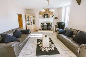 Un salon avec deux canapés en cuir, une cheminée, un meuble en bois et un sol carrelé.