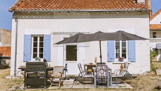 A white building with blue shutters, a tiled roof, and a patio with outdoor furniture. - Annie's Cottage 2Ch fully equipped house (Ribérac)