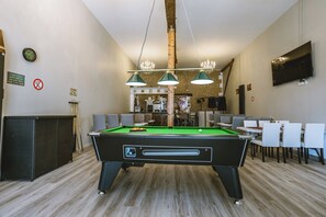 Ein Billardtisch mit drei Lampen, einer Uhr und einem Fernseher an der Wand.