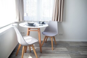 A dining area with a round table, two chairs, and a window with curtains.