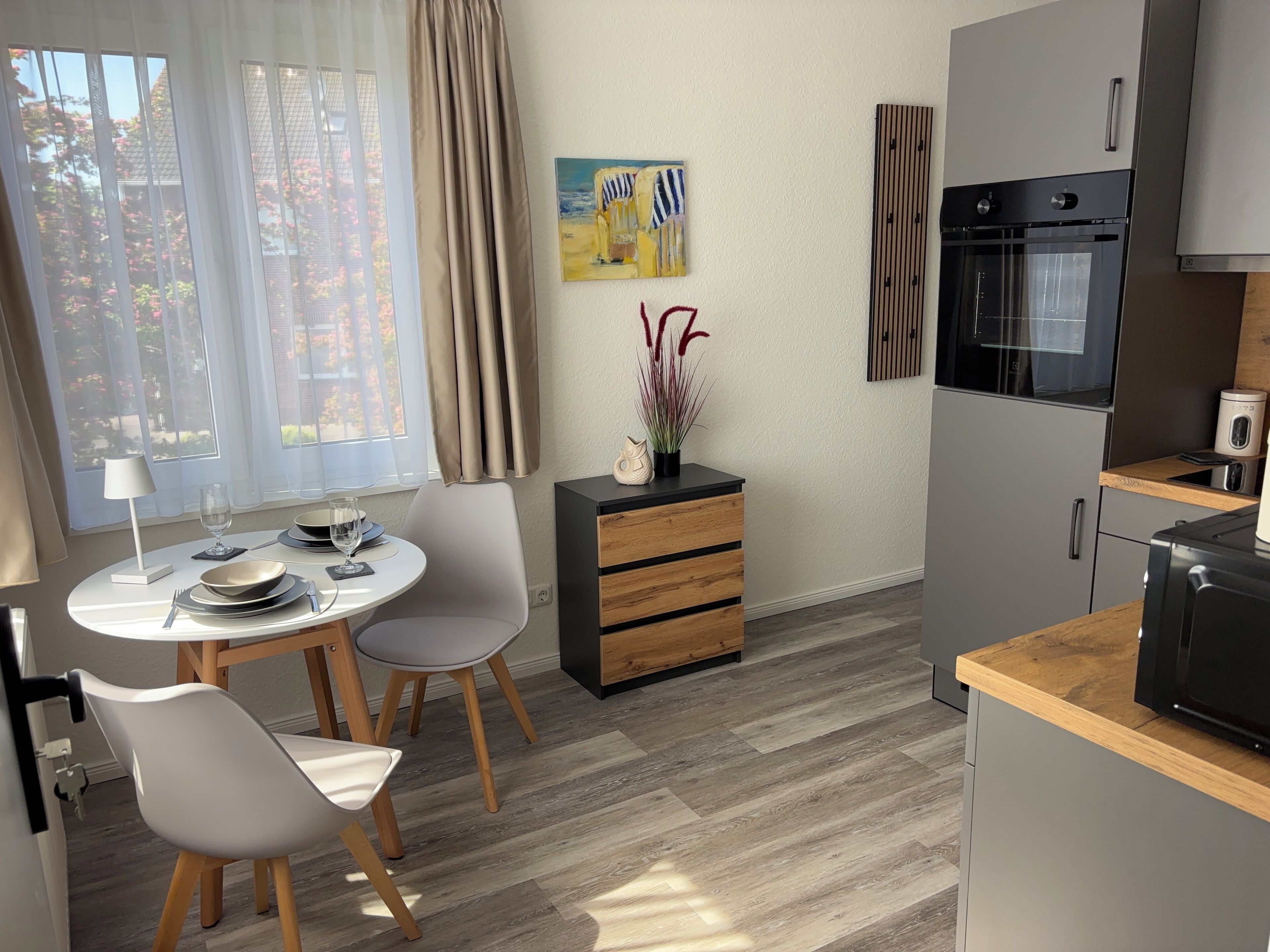 A modern kitchen with a built-in oven, a dining area with a table and chairs, and a view of the outdoors through large windows.