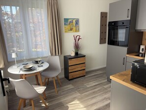 Una cocina moderna con horno integrado, un comedor con mesa y sillas, y vistas al exterior a través de grandes ventanales.