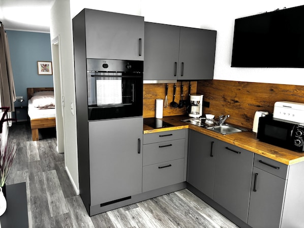 Una cocina compacta con gabinetes grises, encimera de madera, horno empotrado, cafetera y microondas.