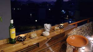 En balkon med gelænder i træ, to barstole, en flaske, et lys og et glas.