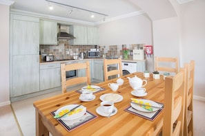 Een moderne keuken met lichte houten kastjes, een magnetron en een ontbijtgedekte eettafel.