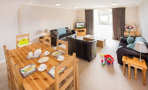 Een ingerichte woonkamer met een eettafel gedekt voor een maaltijd, een bank, een televisie en een raam met gordijnen.
