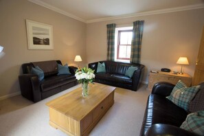 A living room with two sofas, a coffee table, a lamp, a window with curtains, and a framed picture on the wall. - Holstein Cottage The Dairy at Daviot (Inverness-shire)