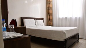 A hotel room with a bed, a bedside table, a water bottle, a glass, and a red chair. - Hotel Twin Towers (Homa Bay)