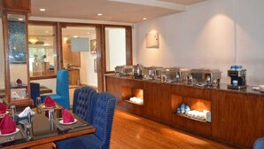 Comedor de hotel con mostrador de buffet, sillas tapizadas en azul y suelo de madera.