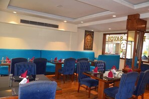A restaurant with blue upholstered booths, wooden tables, and chairs. - Hotel Royal Savoy (Srinagar)