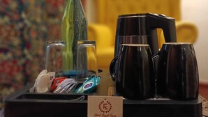 Una bandeja con una cafetera, dos tazas negras, una botella verde y algunos bocadillos.