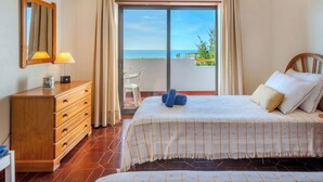 Quarto com cama, cômoda, espelho e vista para o mar.