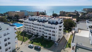 Um hotel com vários andares, piscina no terraço, estacionamento e vista para o mar.