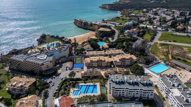 Vista aérea de um resort costeiro com um grande hotel, piscinas e uma praia.