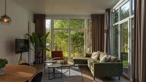 A modern living room with a large window, a sofa, a chair, a coffee table, and a TV. - Vacation Home with Charming Porch (Zuna)