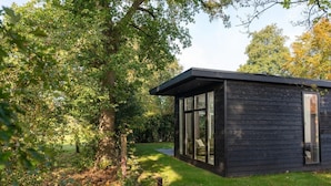 A modern wooden cabin with large windows, surrounded by lush greenery. - Vacation Home with Charming Porch (Zuna)