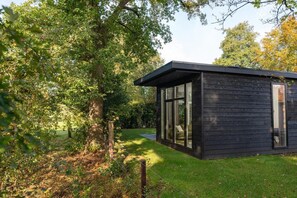 Een moderne houten hut met grote ramen, omgeven door weelderige begroeiing.