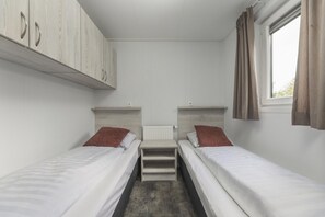 Een nette, kleine kamer met twee eenpersoonsbedden, een radiator en een raam met gordijnen.